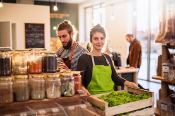 young adult workers in organic store green apron and mason jars of seasoning